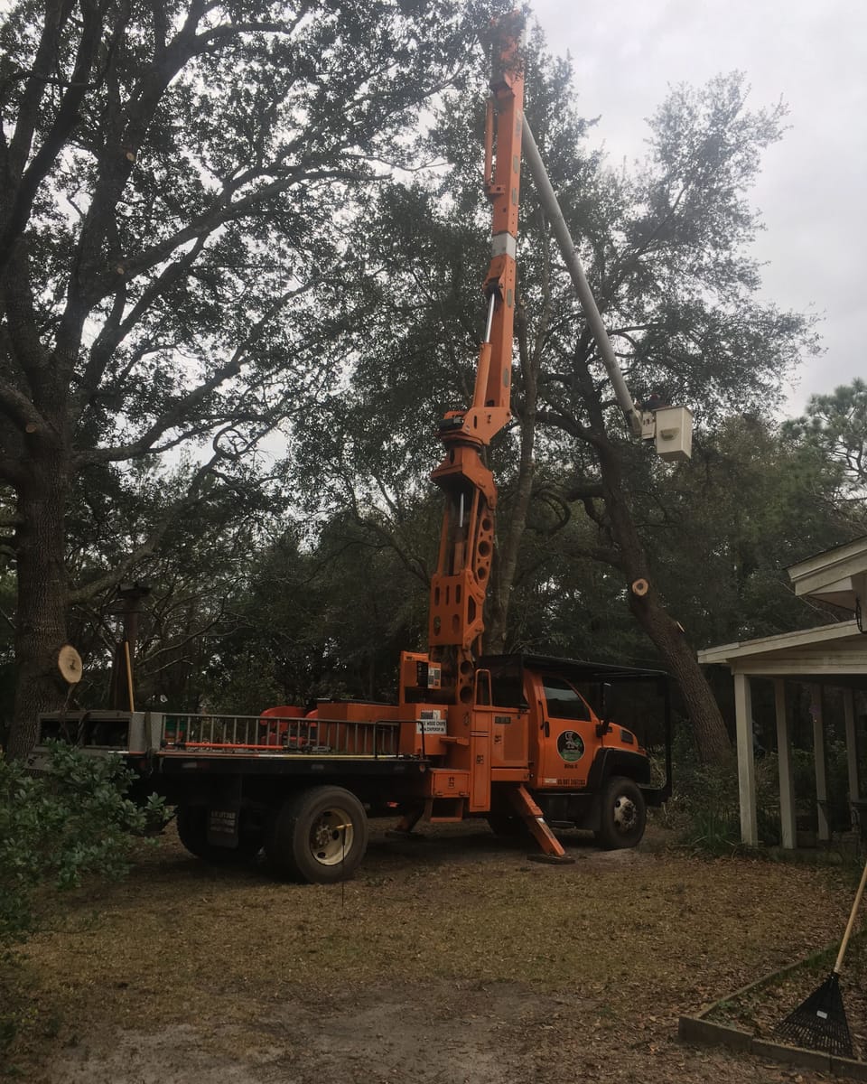 The orange bucket truck parked under a big oak beside a house, boom folded, at the end of a job