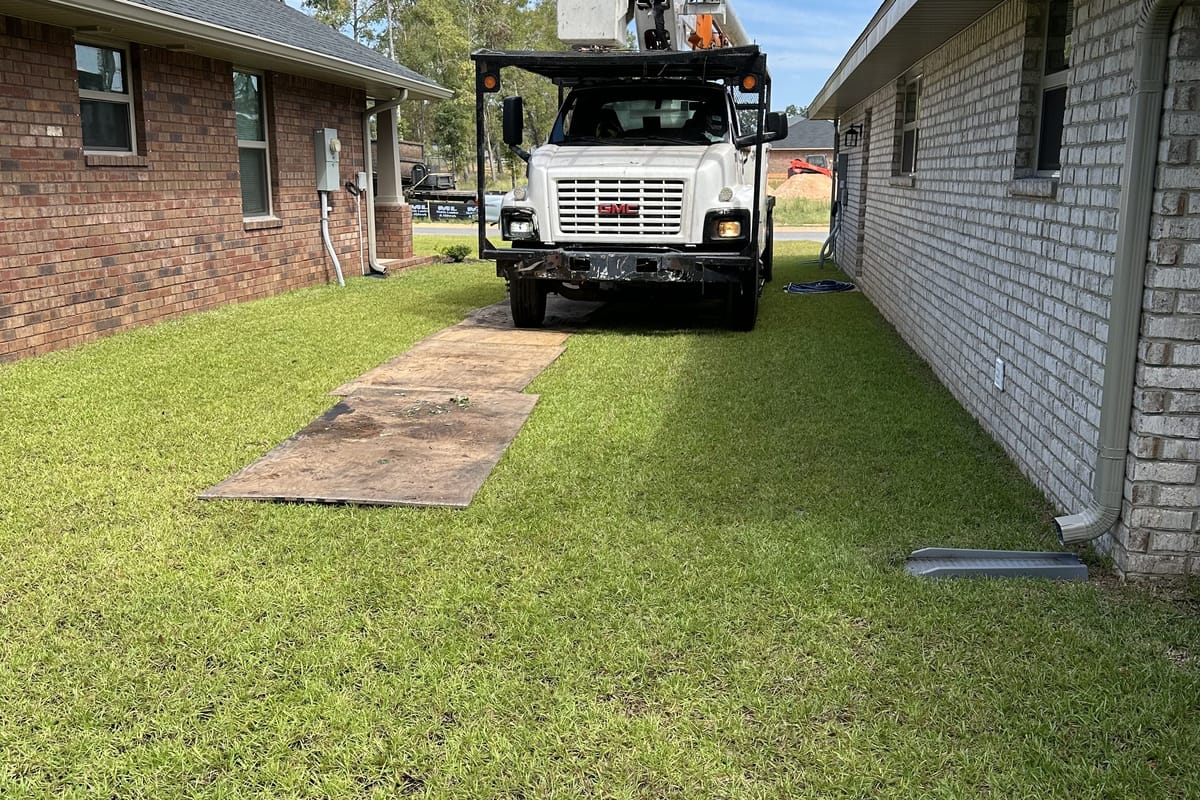 A bucket truck backed down a narrow side yard between two houses on ground mats