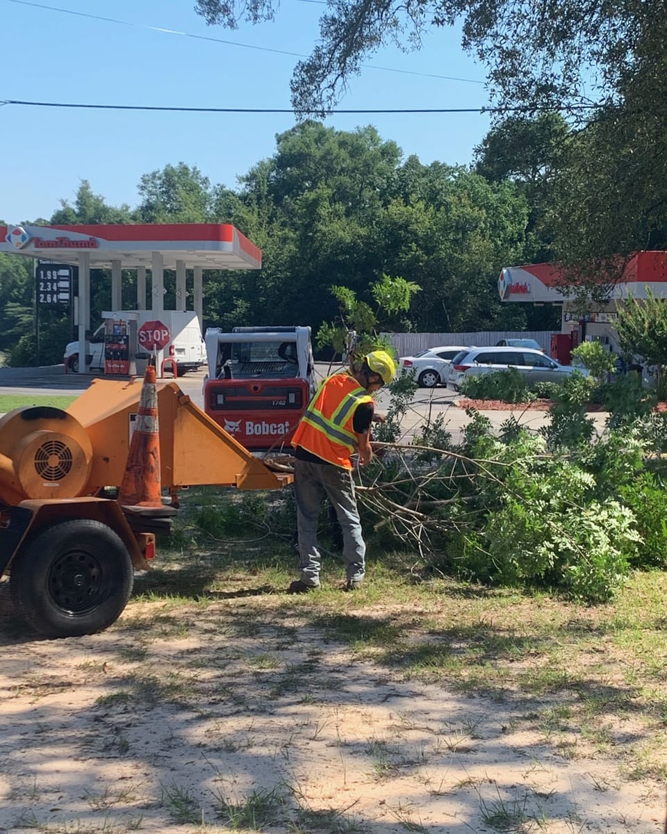 A crew member in a safety vest feeding limbs into the chipper beside the truck