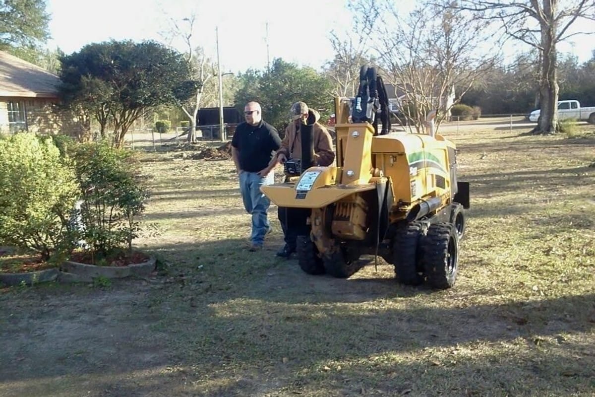Two crew members standing with the yellow stump grinder on a lawn after grinding
